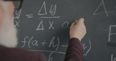 Üst düzey profesör sınıfta araştırma yaparken el yazısı formülünü tahtaya yakın plan yap. Akademik eğitim ve bilgi kavramı.