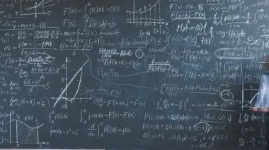 Matematik formüllerini karatahta duvarına yazan zeki bir çocuğun sınıfta hesaplamaya odaklanması. Akademik eğitim ve çocukluk kavramı.