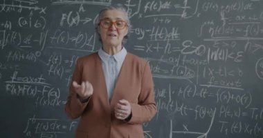 İlham verici bir son sınıf öğretmeninin portresi. Konuşuyor, ders veriyor ve karatahta duvarın yanındaki kameraya bakıyor. Eğitim ve insanlar kavramı.