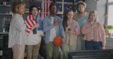 Çeşitli gençlerden oluşan bir grup Amerikan bayrağı taşıyan ve televizyonda spor izleyen ABD milli marşını söyleyen arkadaşlar. Hayranlar ve vatanseverler kavramı.