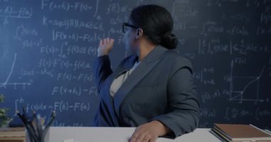 Afro-Amerikalı bayan okul öğretmeninin portresi tahtayı işaret ediyor ve sanal derste kameraya bakıyor. E-öğrenim ve eğitim kavramı.