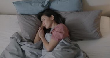 Yatakta battaniyenin altında pijama giyen Asyalı bir kadın akşam keyfine bakıyor. Uyku ve günlük rutin konsept.