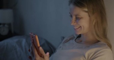 Tasasız genç bayan el sallayarak konuşuyor. Akşamları akıllı telefon ve kablosuz kulaklıkla sanal toplantıdan zevk alıyor. İletişim ve modern teknoloji kavramı.