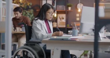 Tekerlekli sandalyede çalışan, masa başında çalışan ve kahve içen hırslı bir bayan. Kapsamlı ofiste çalışmaya odaklanmış. Engelliler ve çalışma alanı kavramı.