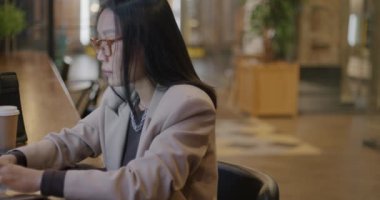 Hırslı Asyalı iş kadını dizüstü bilgisayarla yazı yazıyor ve kafede cep telefonuyla konuşuyor. İş kadını ve profesyonel iletişim konsepti.