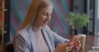 Neşeli genç iş kadını akıllı telefondan ekranlara dokunuyor sonra da kafede müşteriyle konuşuyor. Profesyonel iletişim ve iş konsepti.