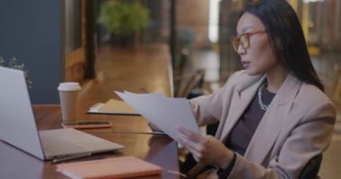 Düşünceli Asyalı iş kadını gazete okuyup kafede dizüstü bilgisayar kullanıyor. Mesleki meslek ve serbest meslek konsepti.