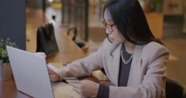 Başarılı Asyalı iş kadını kredi kartı ve dizüstü bilgisayar kullanarak kafede para kazanıyor. Finans ve elektronik bankacılık kavramı.