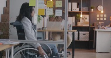 Tekerlekli sandalyeden masaya hareket eden engelli ofis çalışanının yavaş çekim görüntüsü işe hazır. Özel şirket ve engelli çalışan kavramı.