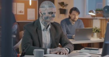 Dövmeli bir ofis çalışanı, akşam iş yerindeki sanal toplantı sırasında bilgisayar konuşmaları ve el kol hareketleriyle çevrimiçi video görüşmesi yapıyor. İletişim ve kapsayıcı çalışma alanı kavramı.