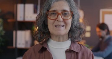 Üst düzey bayan iş danışmanının portresi akşam ofisindeki sanal toplantı sırasında kameraya bakıyor. İletişim ve internet konferansı kavramı.