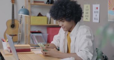 Afro-Amerikalı gençler akıllı telefon kullanarak sosyal medya mesajları okuyor ve evde oturup gülümsüyor. Modern teknoloji ve yaşam tarzı kavramı.