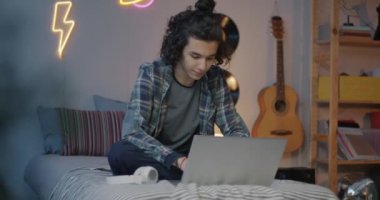 Çift ırklı mutlu genç, bilgisayarlı daktilo kullanıyor. Akşamları yatakta oturuyor. Modern teknoloji ve ergenlik kavramı.