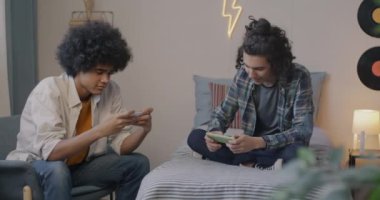 İki genç arkadaş video oyunu oynuyorlar, yarışmanın tadını çıkarıyorlar sonra da yatak odasında el sıkışıyorlar. Arkadaşlık ve eğlence konsepti.