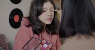 Sevgi dolu anne, kızlarının yüzüne makyaj yapıyor, kızların saçlarını düzeltiyor, evde, yatak odasında güzellik arıyor. Annelik ve tarz kavramı.