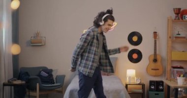 Kablosuz kulaklık takan, müzik dinleyen ve dans eden neşeli ergen çocuk evde, yatak odasında eğleniyor. Gençlik kültürü ve modern yaşam tarzı kavramı.