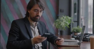Orta Doğulu mutlu işadamı kredi kartı ve akıllı telefon kullanarak kafeden alışveriş yapıyor. İş ve finans kavramı.