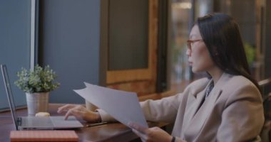 Asyalı iş kadını, dokümanları yağmalıyor ve laptopla birlikte kafede kahve içiyor. İş planlaması ve başarılı kişi konsepti.