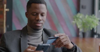 Kafede otururken kredi kartı ve akıllı telefon alışverişi yapan Afrikalı Amerikalı girişimci. Başarılı e-ticaret ve para kavramı.
