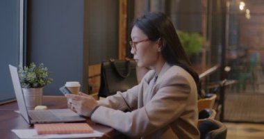 Kendine güvenen Asyalı iş kadını cep telefonuyla konuşuyor. Kafe masasında çalışan profesyonel işbirliğini tartışıyorlar. İletişim ve iş konsepti.