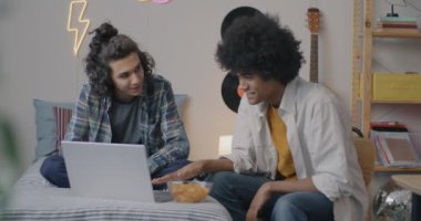 Mutlu ergen çocuklar dizüstü bilgisayarlarını birlikte kullanır konuşurlar ve cips yerler. Evde, yatak odasında vakit geçirirler. Modern teknoloji ve gençlik kavramı.