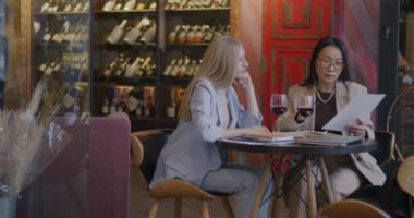 Genç kadın iş ortakları sözleşmeyi tartışıyor belgelere bakıyor ve kafede kağıt tutarak konuşuyorlar. Takım çalışması ve işbirliği kavramı.