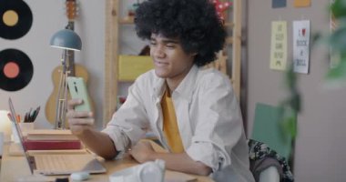 Neşeli Afrikalı Amerikalı ergen akıllı telefonuyla evde el sallayarak çevrimiçi video görüşmesi yapıyor. İletişim ve sanal buluşma kavramı.