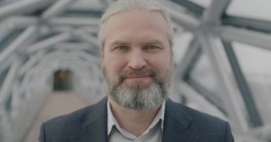 Modern cam salon arka planında kameraya bakarak gülümseyen neşeli, olgun iş adamının yakın plan portresi. İş ve insan kavramı.