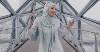 Orta Doğulu neşeli bir iş kadınının, ofis cam koridorunda dans edip müzik dinlemesi. Gençlik kültürü ve eğlence kavramı.