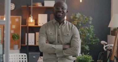 Modern ofiste kollarını kavuşturup kameraya bakarak gülümseyen başarılı Afrikalı Amerikalı iş adamının yavaş çekimde portresi. İş ve iş adamı kavramı.