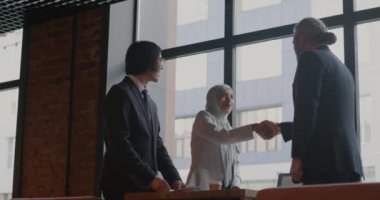 Çok uluslu bir grup iş adamı modern kafede el sıkışıyor ve içeride konuşuyor. İş toplantısı ve ortaklık kavramı.