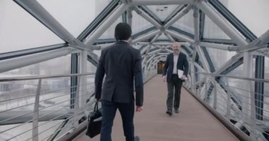 Ofis binasının modern cam koridorunda el sıkışan iki işadamının yavaş çekimde buluşması. İş ve insan kavramı.