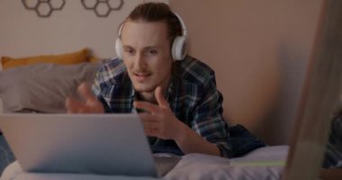 Neşeli adam müzik dinliyor, dans ediyor ve dizüstü bilgisayarla evde yatıyor. Serbest çalışma ve gençlik kültürü kavramı.