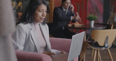 Dizüstü bilgisayarla çalışan neşeli Orta Doğulu iş kadını kafedeki koltukta oturarak online etkinliğe odaklanmış durumda. Bilgisayar ve iş konsepti.