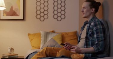 Neşeli genç adam TV 'de komik bir program izliyor. Evde oturmuş cipsleri yiyor ve gülüyor. Televizyon ve eğlence konsepti.