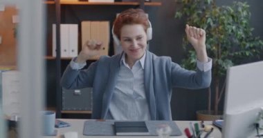 Neşeli ofis çalışanı müzik dinliyor iş yerinde kulaklıkla eğleniyor. Modern teknoloji ve eğlence konsepti.