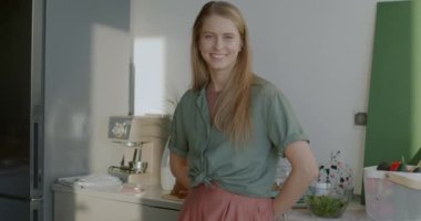 Mutfakta durup kameraya gülümseyen güzel bir genç kadının yavaş çekim portresi. İnsanlar ve apartman kavramı.