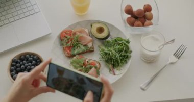 Akıllı telefonla yakın plan çekimde masada lezzetli sağlıklı yemeklerin fotoğraflarını çekerken çevrimiçi blog ve sosyal medya için fotoğrafçılığa odaklandık. Beslenme ve gıda bloglama kavramı.