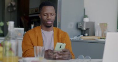 Akıllı telefon kullanan neşeli Afro-Amerikan bir adamın yavaş çekimde portresi. Sonra kameraya bakıp evde otururken gülümsemesi. Gadget ve insanlar konsepti.