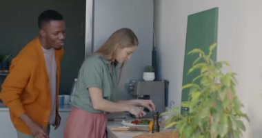 Genç bir kadının mutfakta yemek pişirmesi yavaş çekimde eğlenceli bir koca gelip sarılırken. Beslenme ve ilişki kavramı.