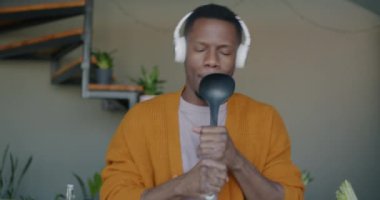Neşeli Afrikalı Amerikalı adamın kulaklıkla müzik dinlemesi, dans etmesi ve evdeki hayali mikrofonda şarkı söylemesi.