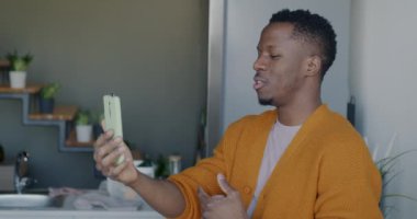 Gamsız Afrikalı Amerikalı akıllı telefon ekranına bakarak konuşuyor. Evdeki mutfakta çevrimiçi video görüşmesi yapıyor. Sanal toplantı ve uzaktan iletişim konsepti.