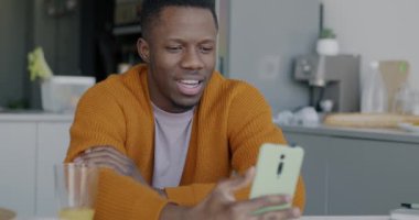 Akıllı telefonuyla online video görüşmesi yapan mutlu Afro-Amerikalı adam evde mutfaktaki sanal toplantının keyfini çıkarıyor. İletişim ve insan kavramı.