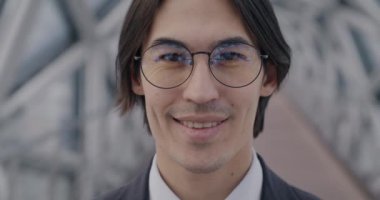 Modern cam salonda kameraya gülümseyen Asyalı iş adamının yavaş çekim portresi. İş ve duygu kavramı.