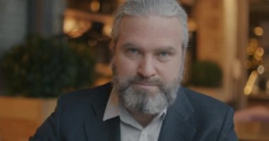 Zarif takım elbiseli olgun bir girişimcinin rahat bir kafede kameraya bakışının yavaş çekim portresi. İş adamı ve hedefler konsepti.