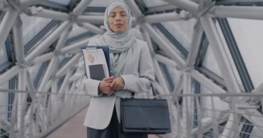 Modern cam salonda duran tesettürlü, tesettürlü ve tesettürlü Orta Doğulu kadının yavaş yavaş portresi. Kameraya bakıp gülümsüyor.
