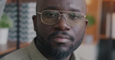 Ciddi bir Afrikalı Amerikalının ofis arka planında kameraya bakarken yavaş çekimde çekilmiş portresi. İş adamı ve şirket kavramı.