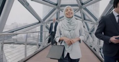 Orta Doğulu tesettürlü, tesettürlü bir iş kadınının ofis binasının camlı geçidinde yürümesi. İş adamı ve çalışma alanı kavramı.