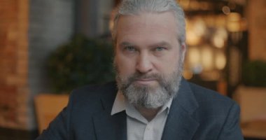Kafenin içinde ciddi bir yüzle kameraya bakan zarif bir iş adamının yavaş çekim portresi. Başarılı iş adamı ve duygu konsepti.