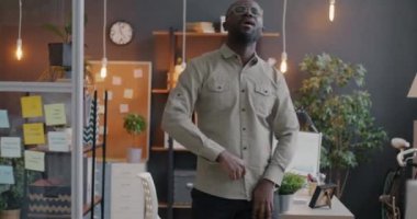 Afrika kökenli Amerikalı neşeli iş adamlarının yavaş çekimleri dans edip şarkı söylemeleri işyerinde rahatlatıcı müzik dinlemeleri. Eğlence ve iş konsepti.